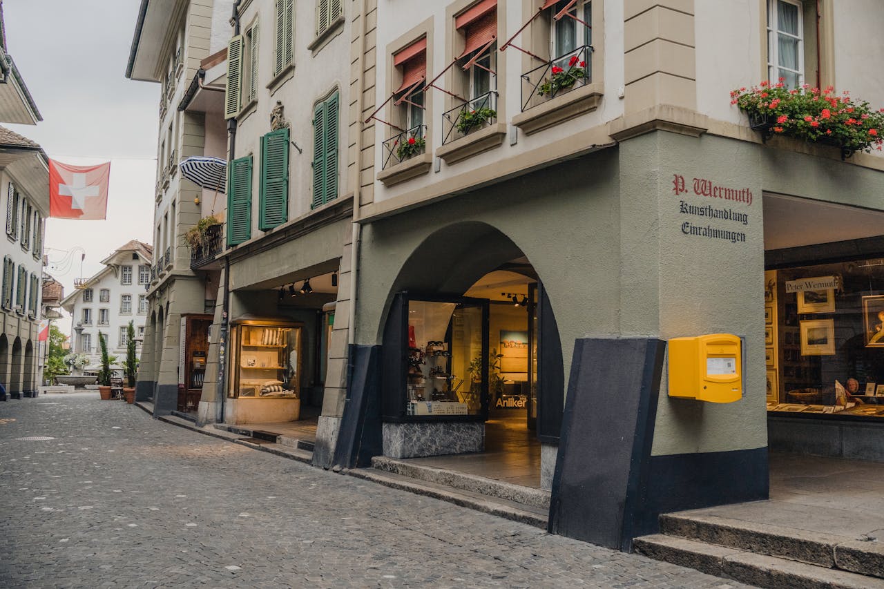 Cobblestone street in Thun, Switzerland, featuring traditional architecture and Swiss flags.