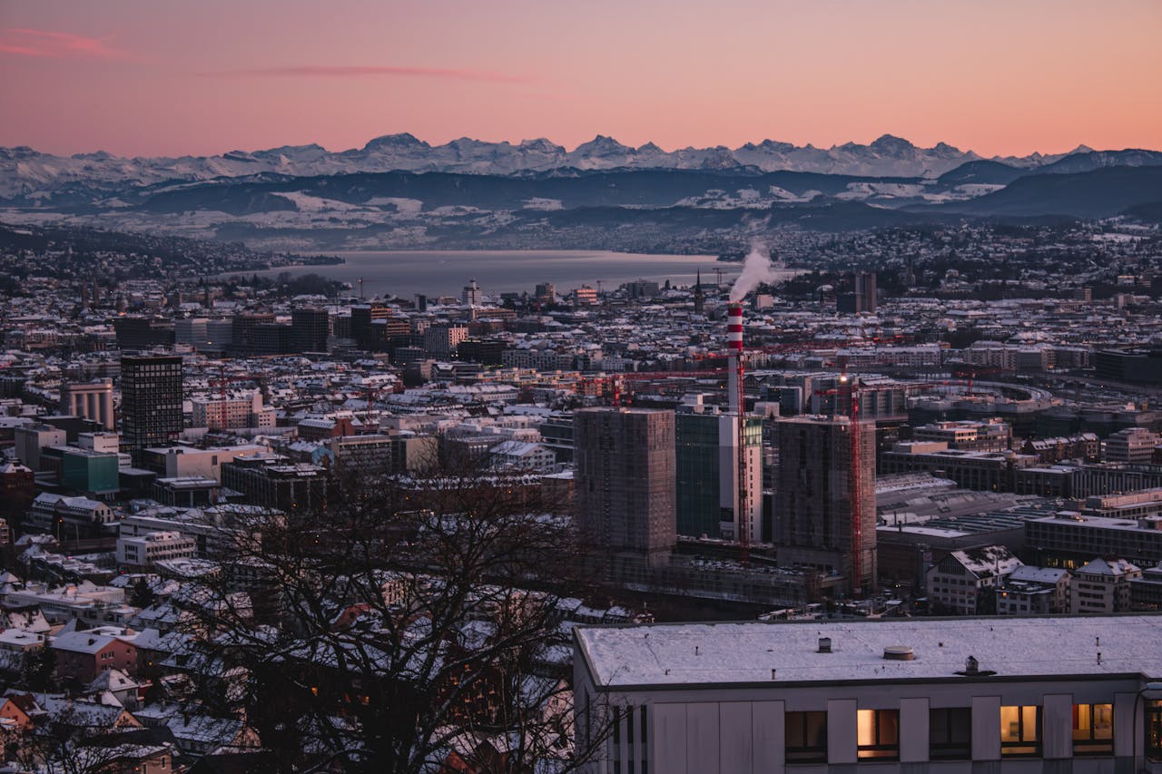 Aerial view of Zürich cityscape at winter sunset with snowy Alps backdrop.