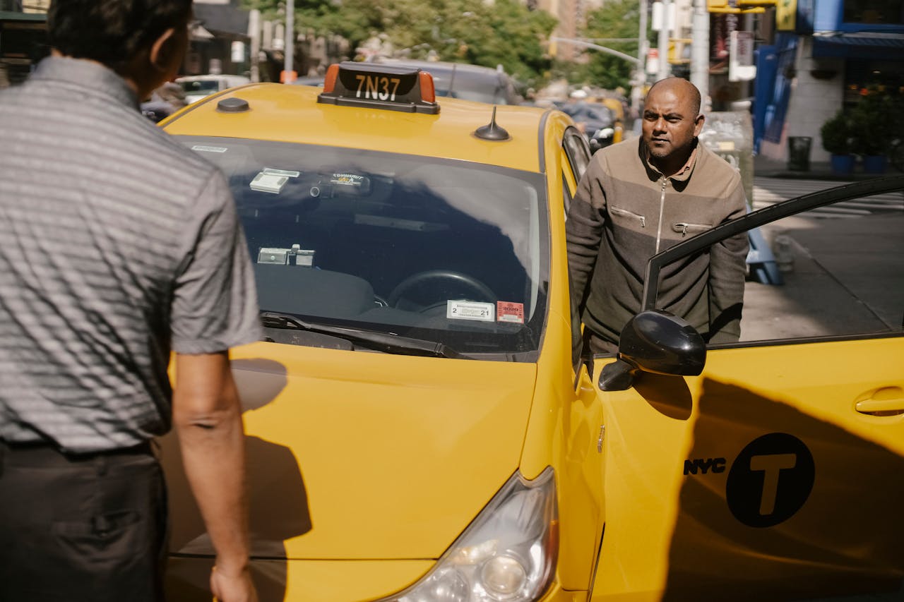 Serious ethnic cab driver having conversation with man in sunny day in New York